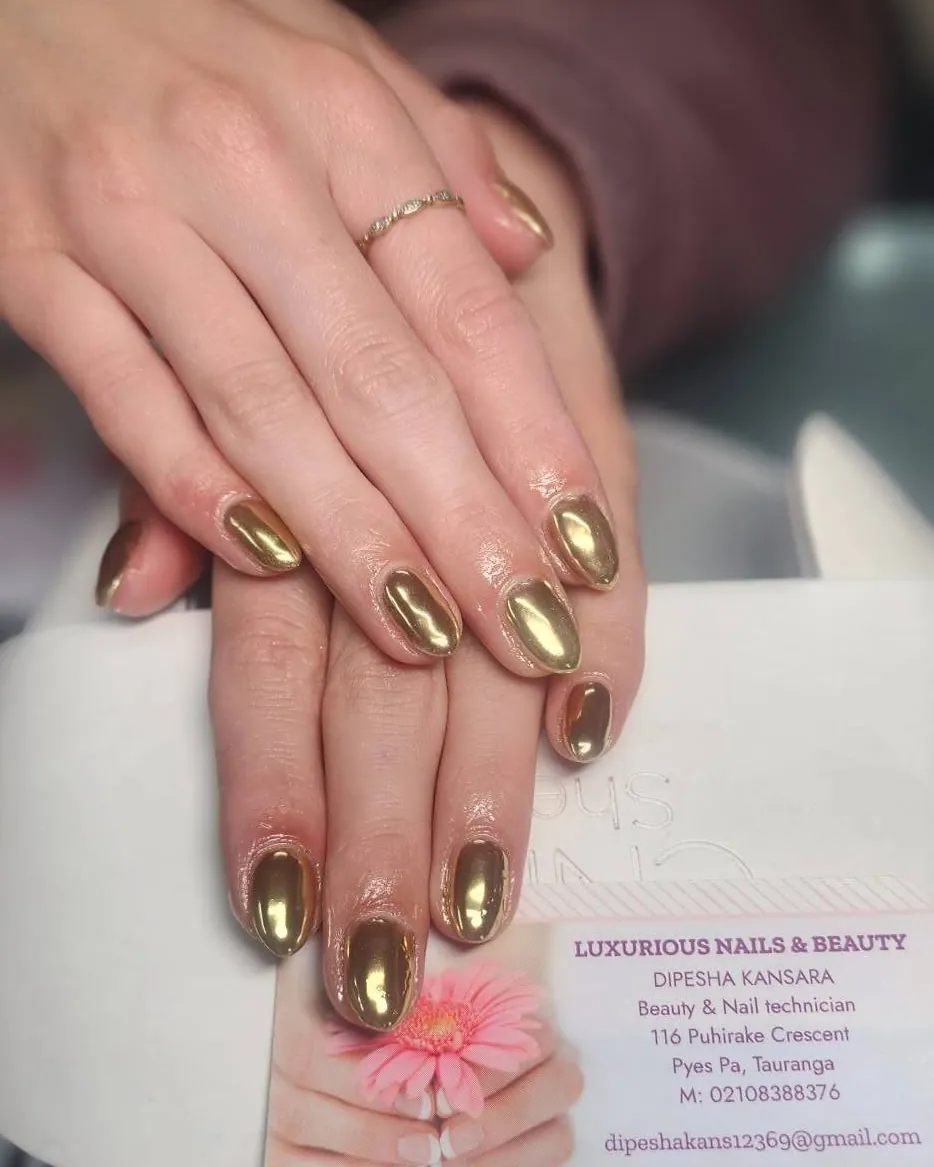 Gold chrome gel nails on a client's hands, over the salon business card