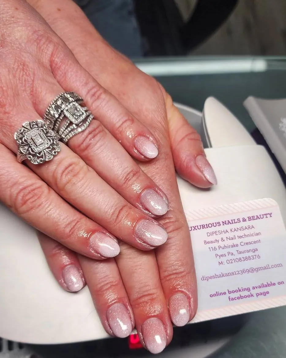 A client's pearl-finish gel manicure, resting on a Luxurious Nails and Beauty business card at the nail desk